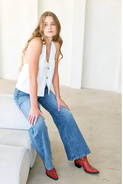Woman wearing a white sleeveless top, blue jeans, and red shoes sitting on a white couch.