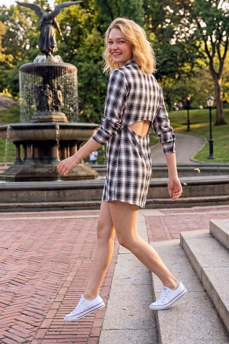 Woman in a plaid dress walking in a park with a fountain in the background
