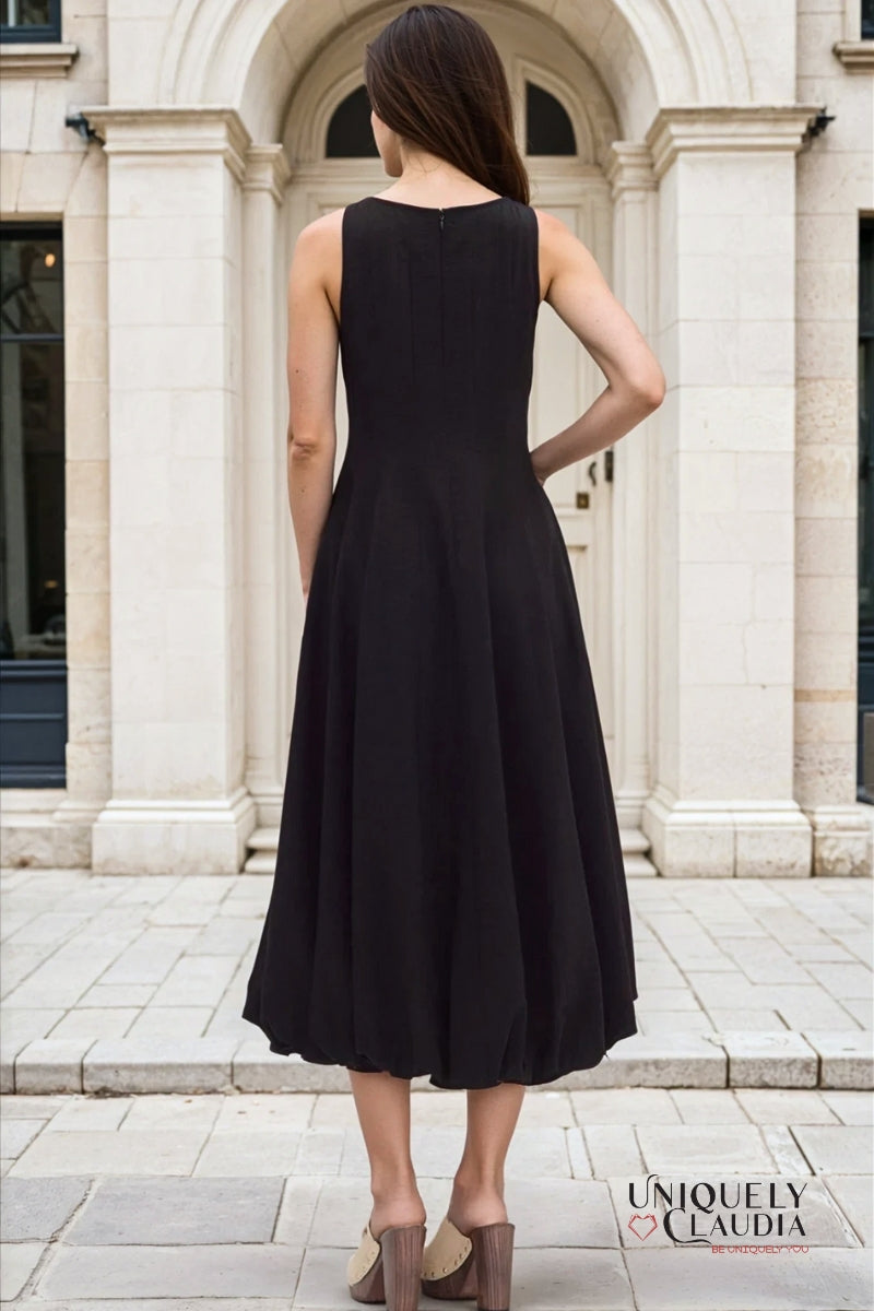 Woman wearing a black dress standing in front of a building with columns.