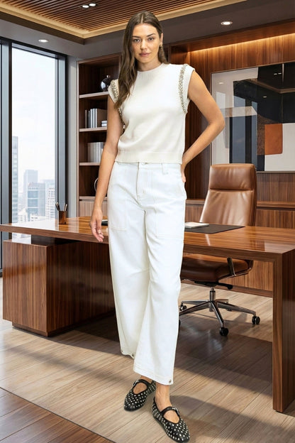 Woman in a white outfit standing in an office setting with wooden furniture and large windows.