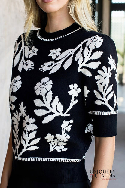 Black sweater with white floral patterns worn by a person indoors.