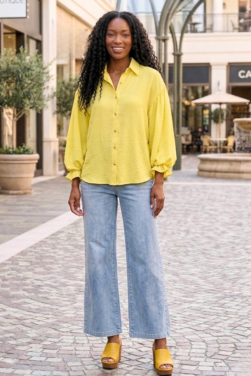Woman wearing a yellow blouse and blue jeans standing on a paved walkway.
