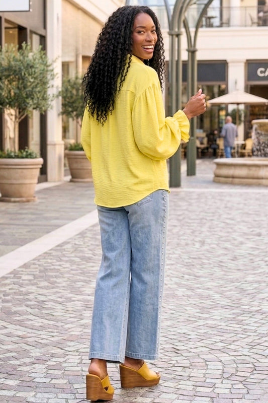Woman in yellow top and blue jeans standing on a street with shops in the background