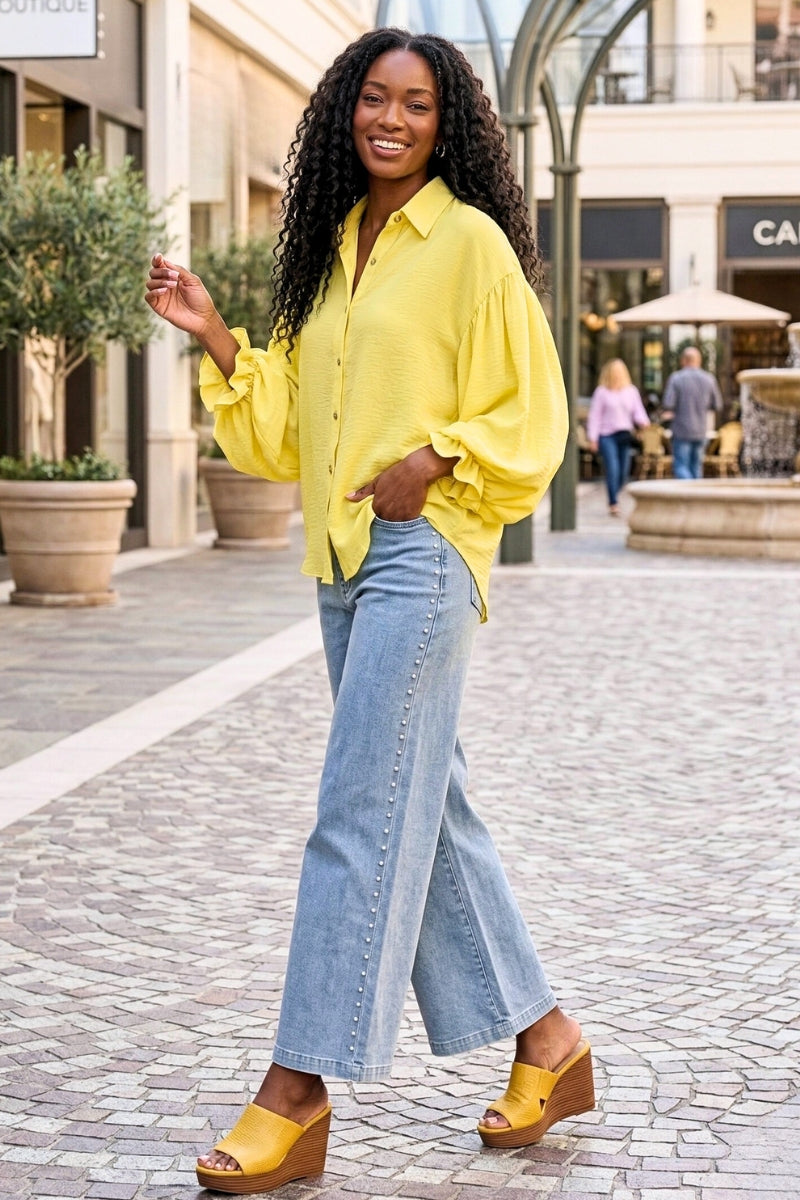 Woman in yellow shirt and blue jeans standing on a street with shops in the background