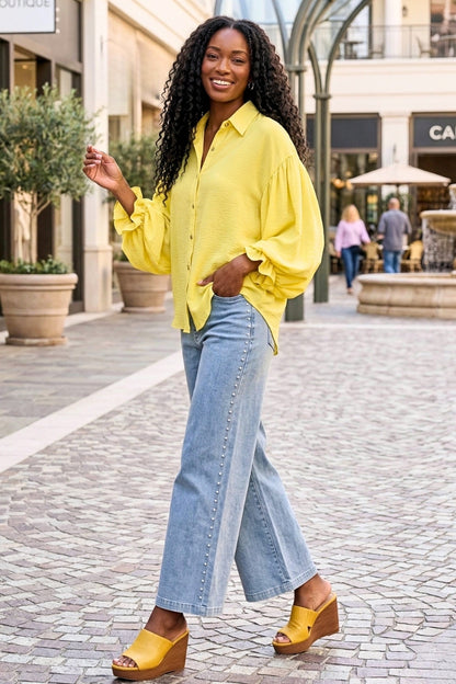 Woman in yellow shirt and blue jeans standing on a street with shops in the background