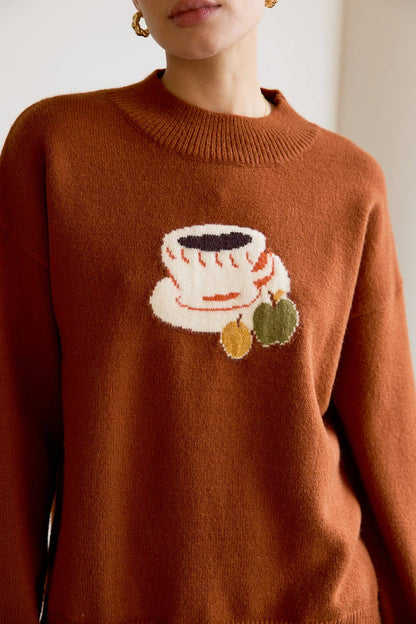 Brown sweater with a coffee cup and cookies design worn by a person.