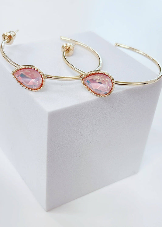 Gold hoop earrings with pink gemstones on a white stand