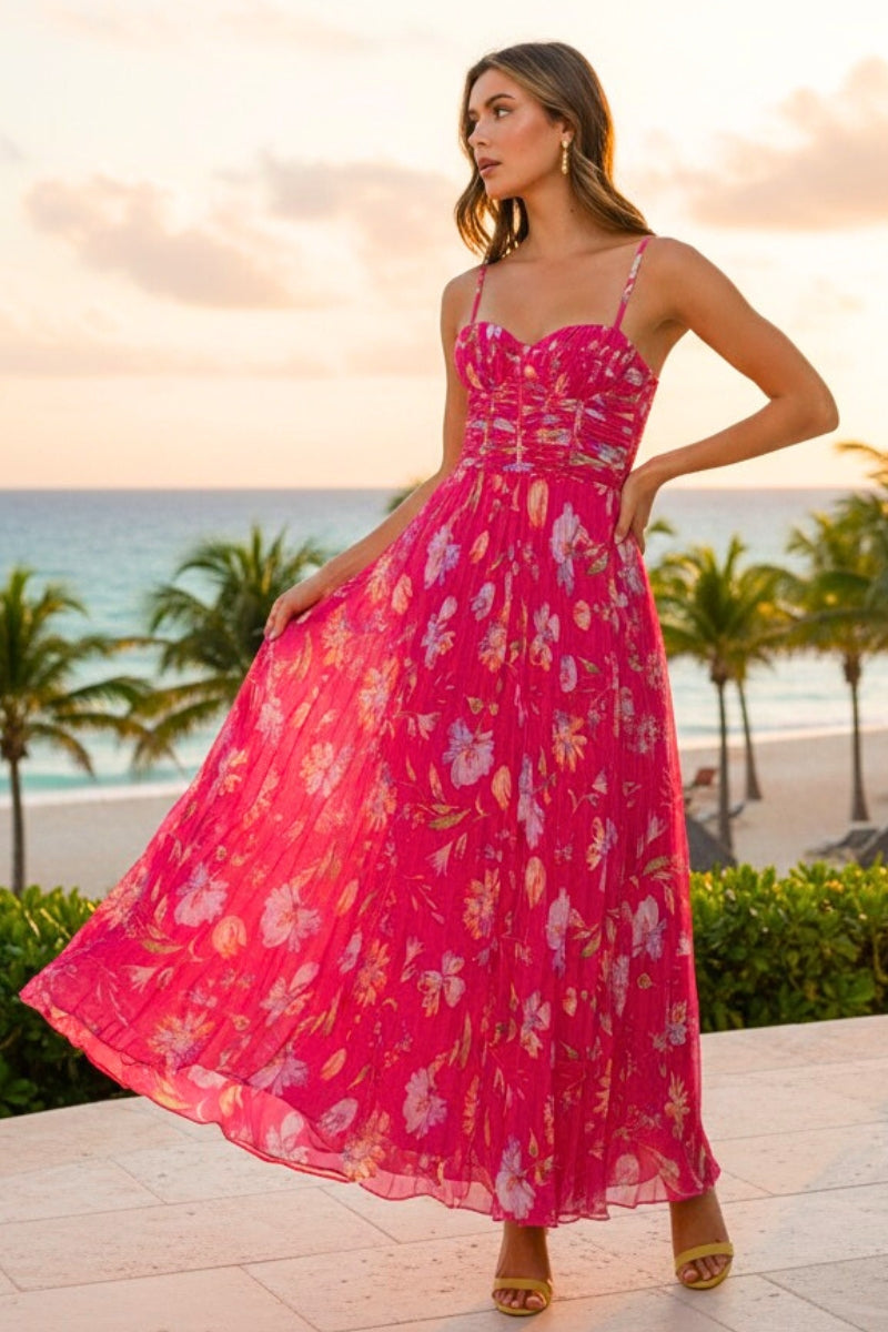 Woman in a pink floral dress standing on a beach at sunset