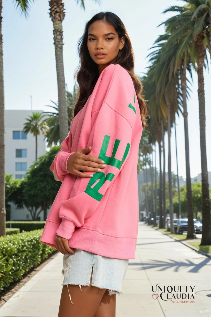Woman wearing a pink sweatshirt with green text on a palm tree-lined street.