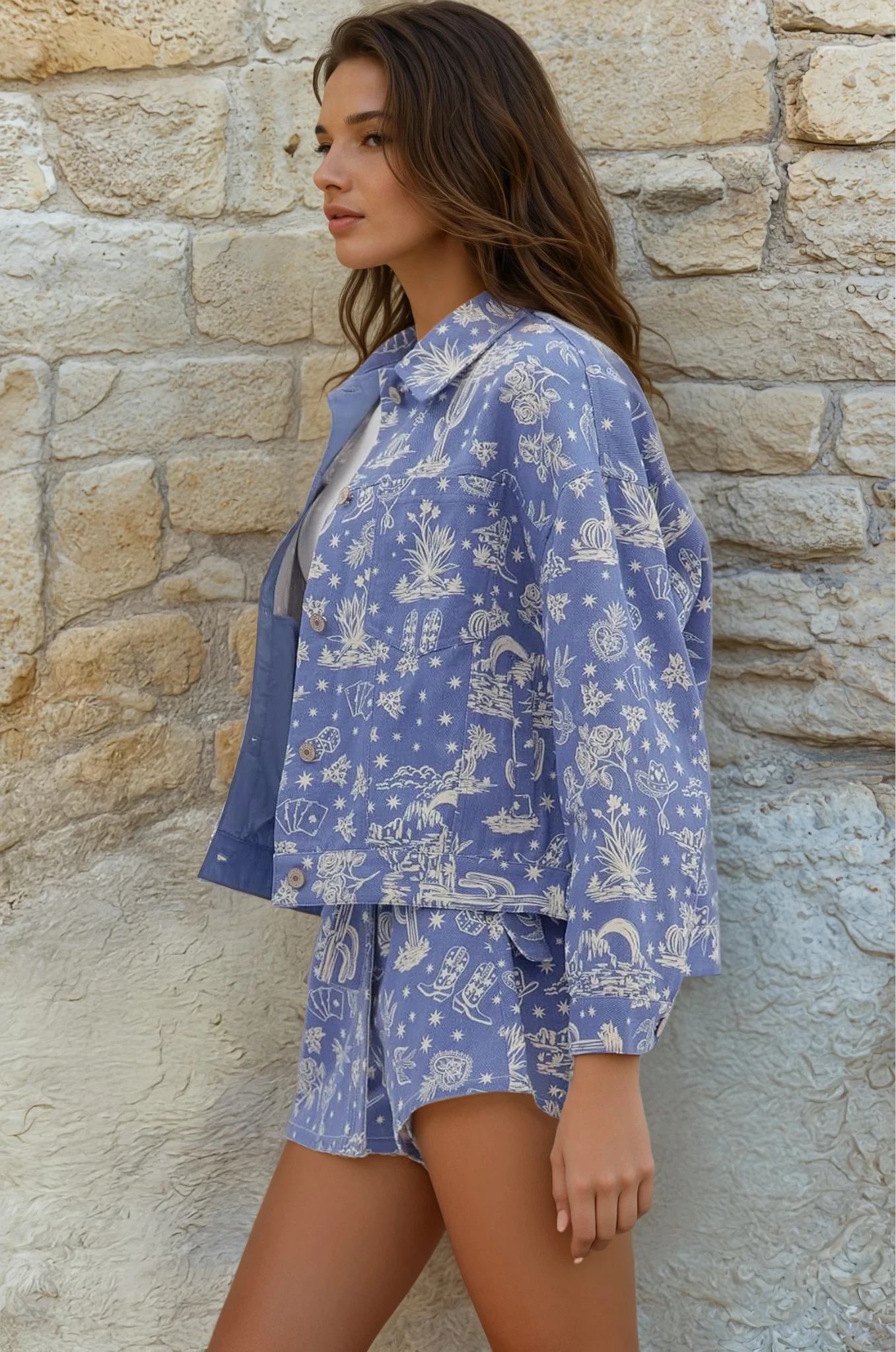 Woman wearing a blue patterned outfit standing against a stone wall.