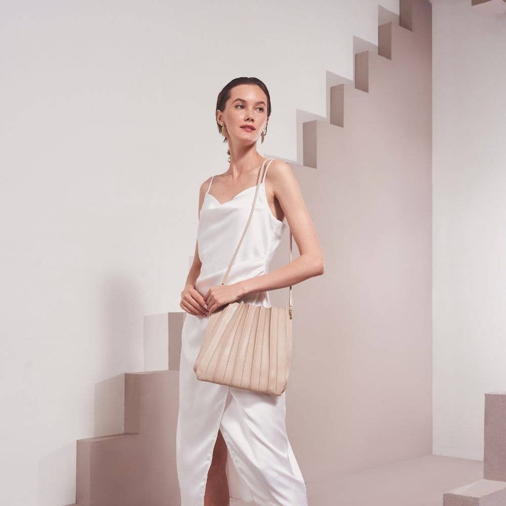 Woman in a white outfit holding a beige handbag on a minimalistic background
