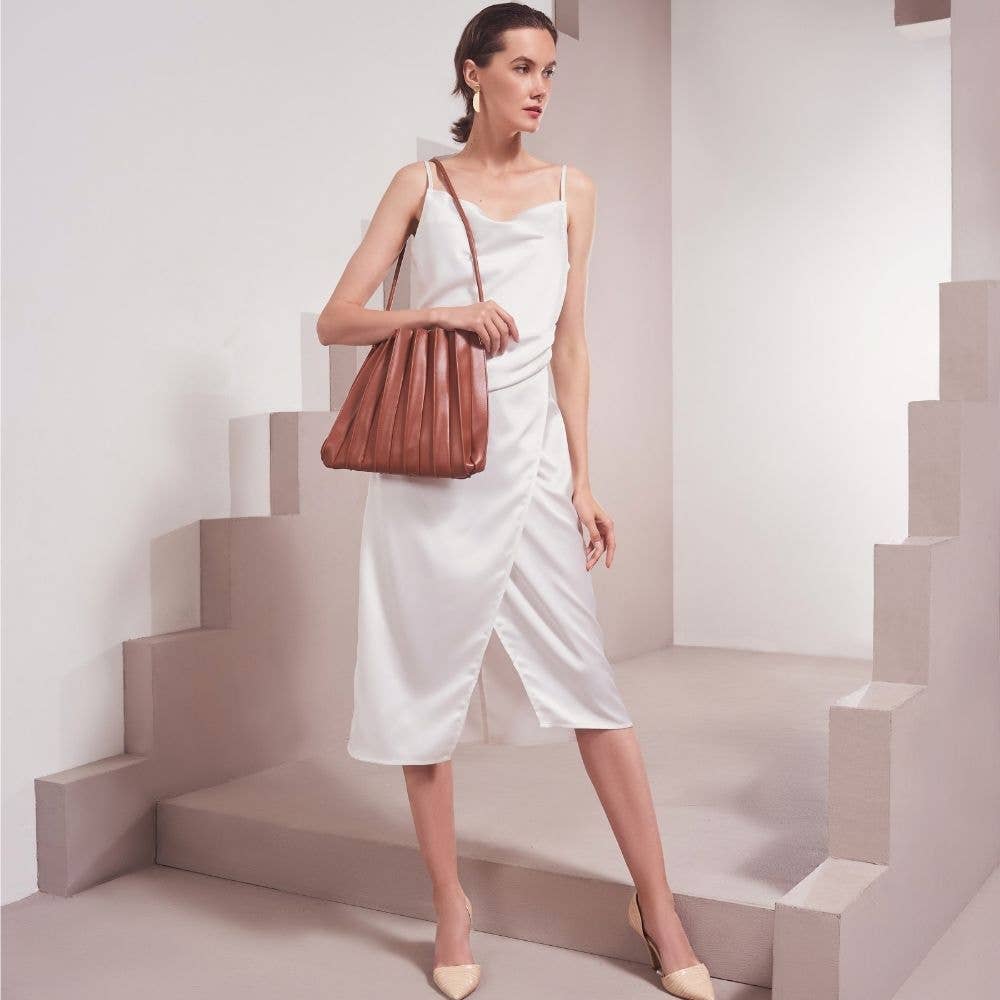 Woman in a white dress holding a brown leather handbag on a geometric staircase.