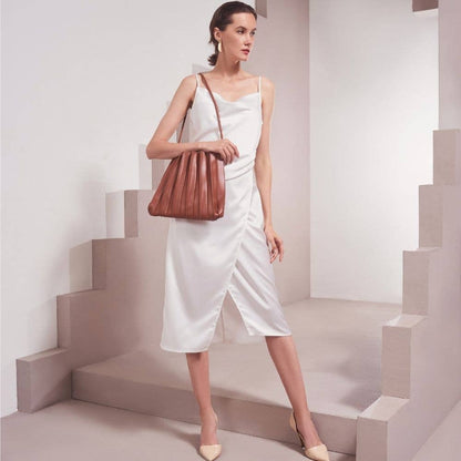 Woman in a white dress holding a brown leather handbag on a geometric staircase.