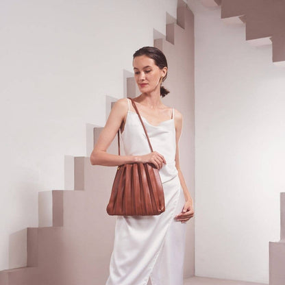 Woman holding a brown leather handbag in a minimalistic setting