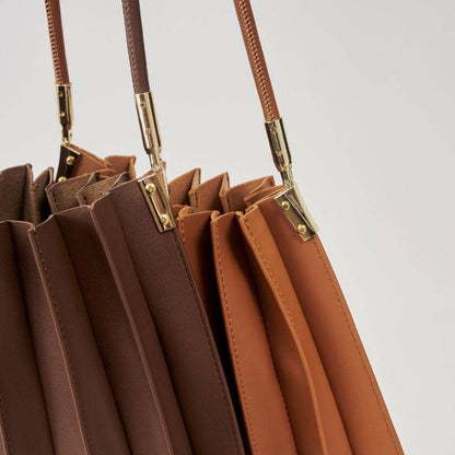 Close-up of brown leather handbags with gold hardware on a light gray background