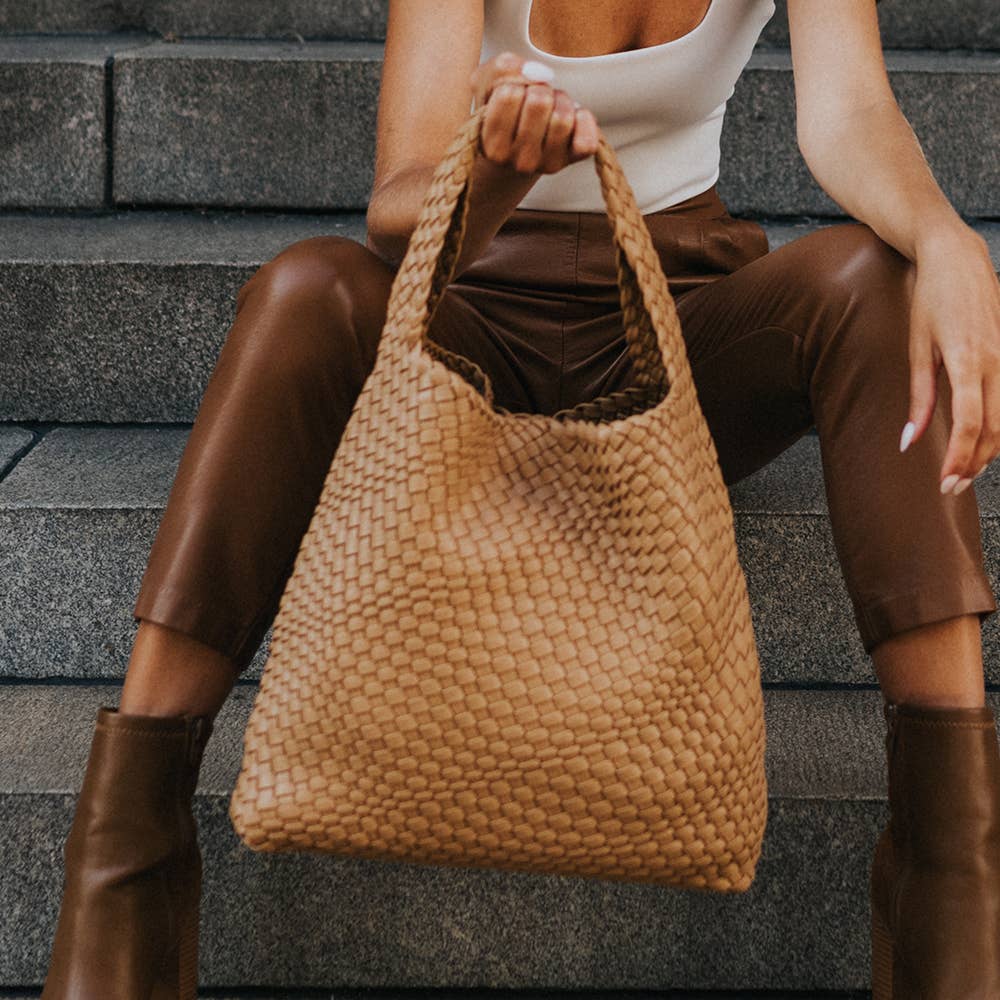 Person sitting on steps holding a woven camel bag