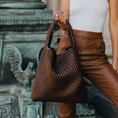 Person holding a woven brown handbag with a classical sculpture in the background