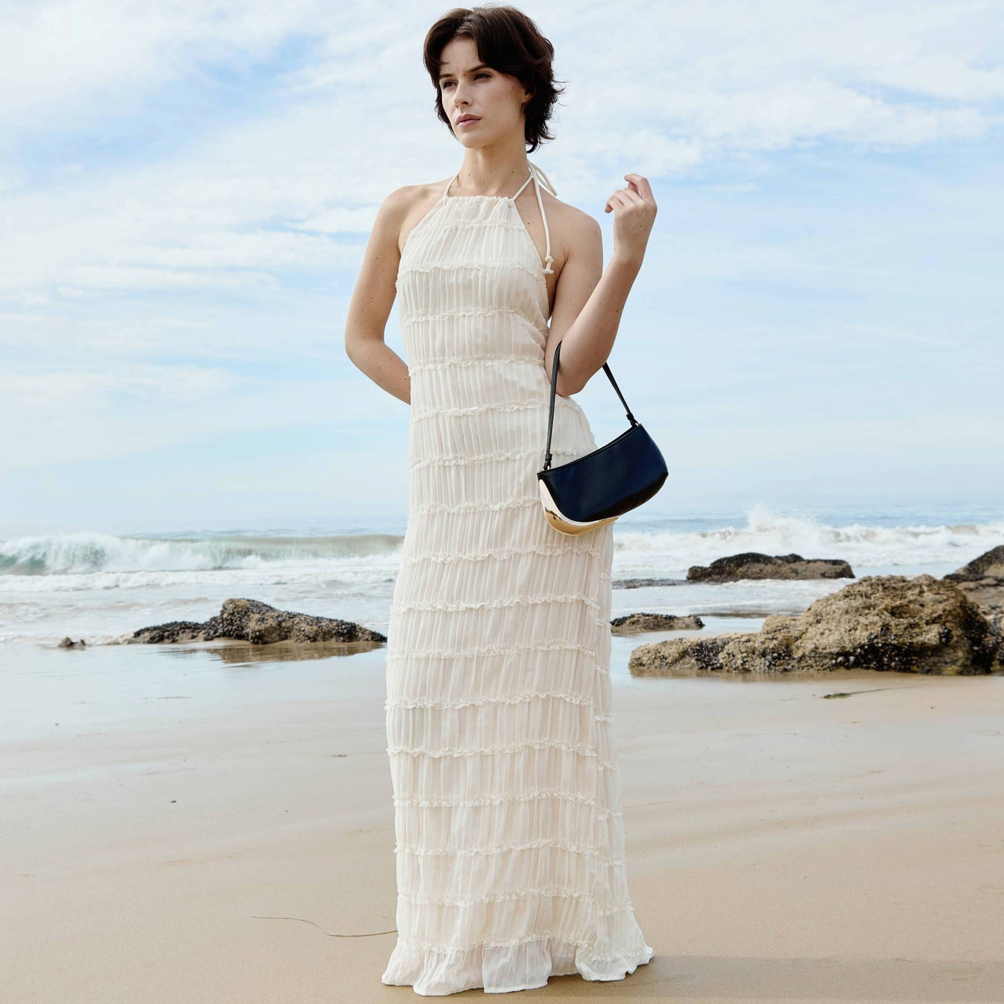 Woman in a long white dress holding a blue handbag on a beach
