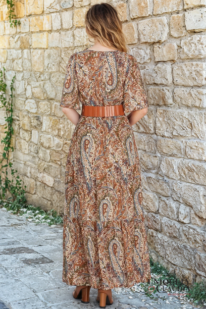 Woman wearing a patterned dress standing against a stone wall.