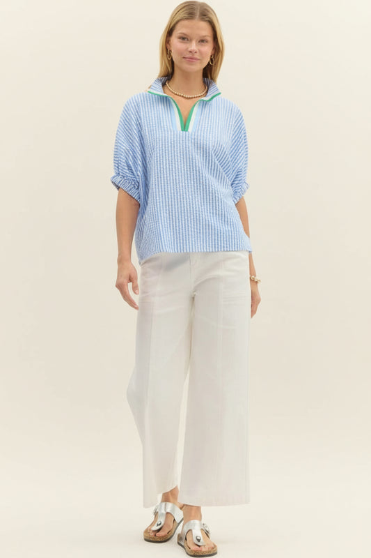 Woman wearing a blue and white striped shirt with a green trim, standing against a plain background.