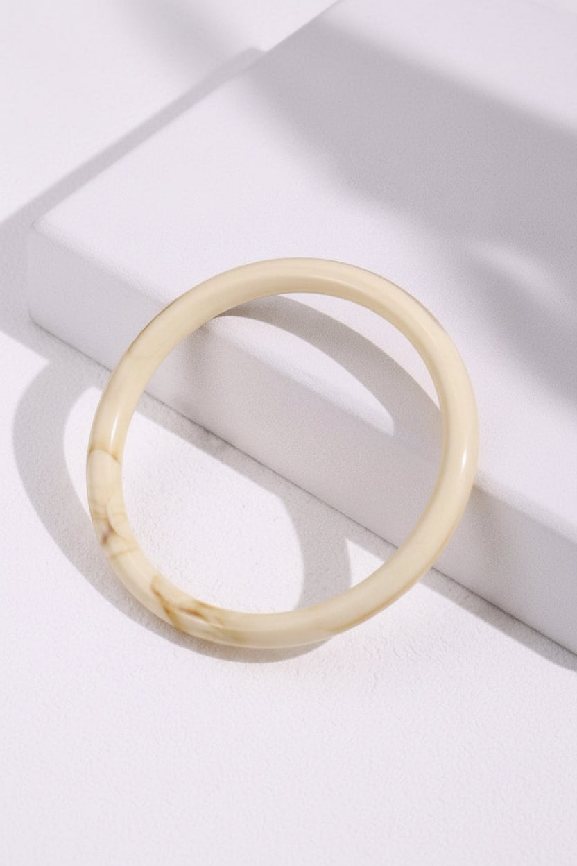 Beige bracelet on a white surface with green leaves