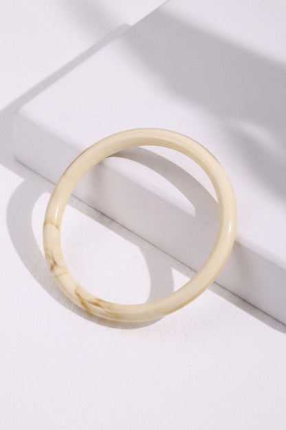 Beige bracelet on a white surface with green leaves
