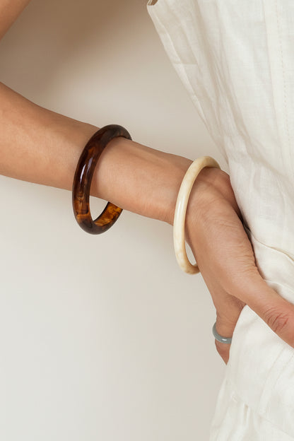 Close-up of a person's arm wearing two bracelets against a neutral background