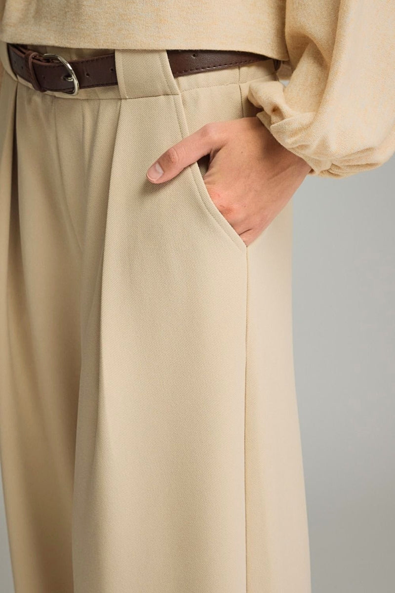 Close-up of beige pants with a hand in the pocket against a neutral background