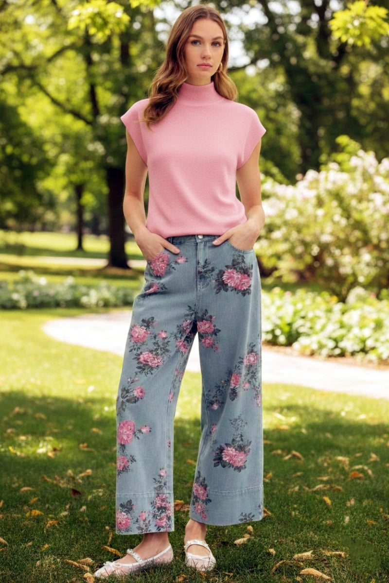 Woman wearing a pink top and floral pants standing in a park.