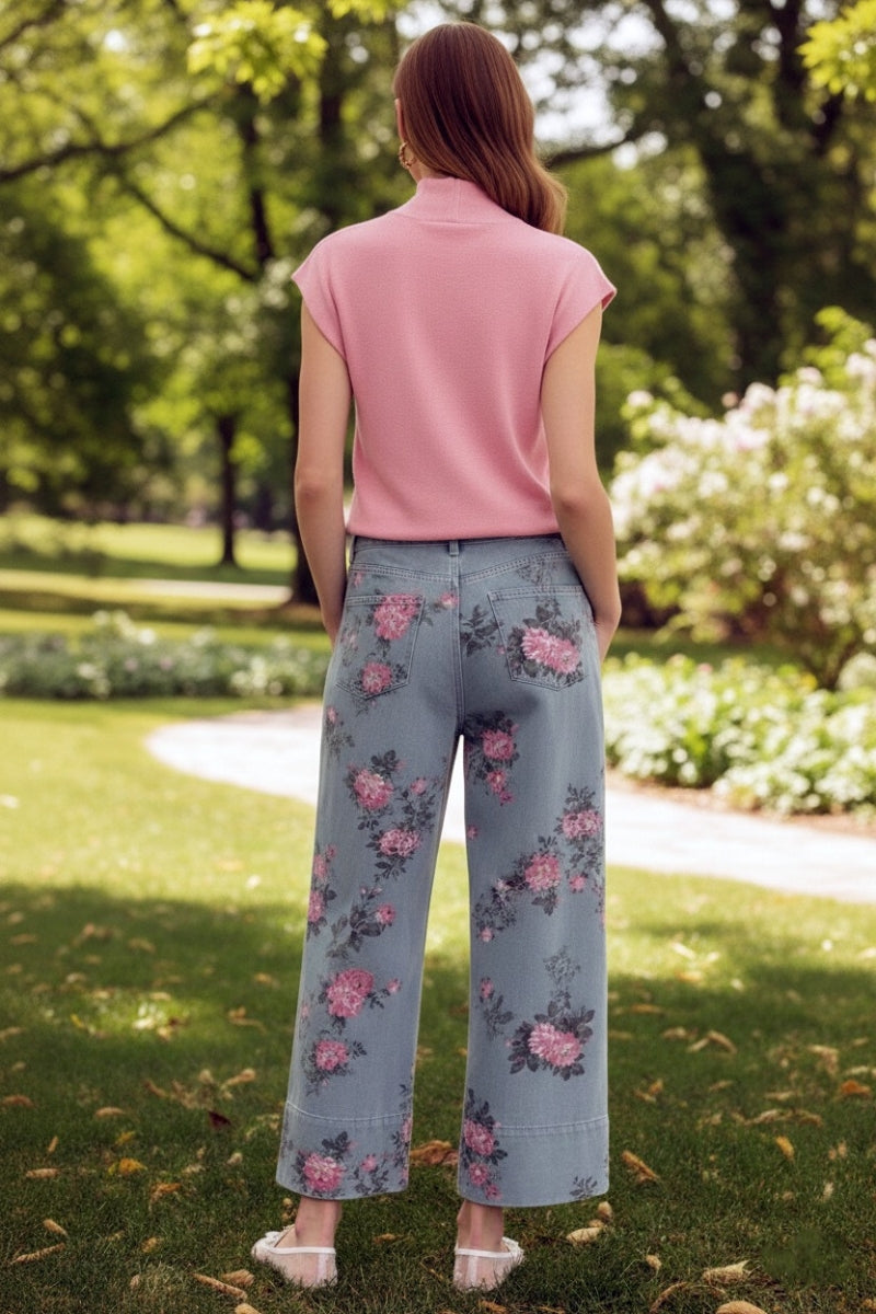 Woman wearing a pink top and floral pants standing in a park.