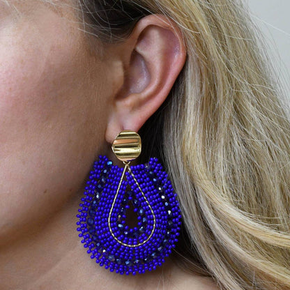 Close-up of a person wearing a blue beaded earring with a gold accent.