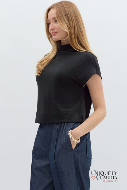 Woman wearing a black top and navy pants on a light gray background with 'Uniquely Claudia' branding.