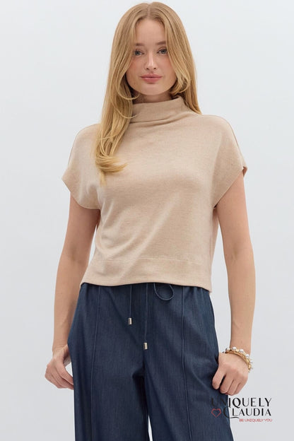 Woman wearing a beige turtleneck top and dark blue pants on a white background
