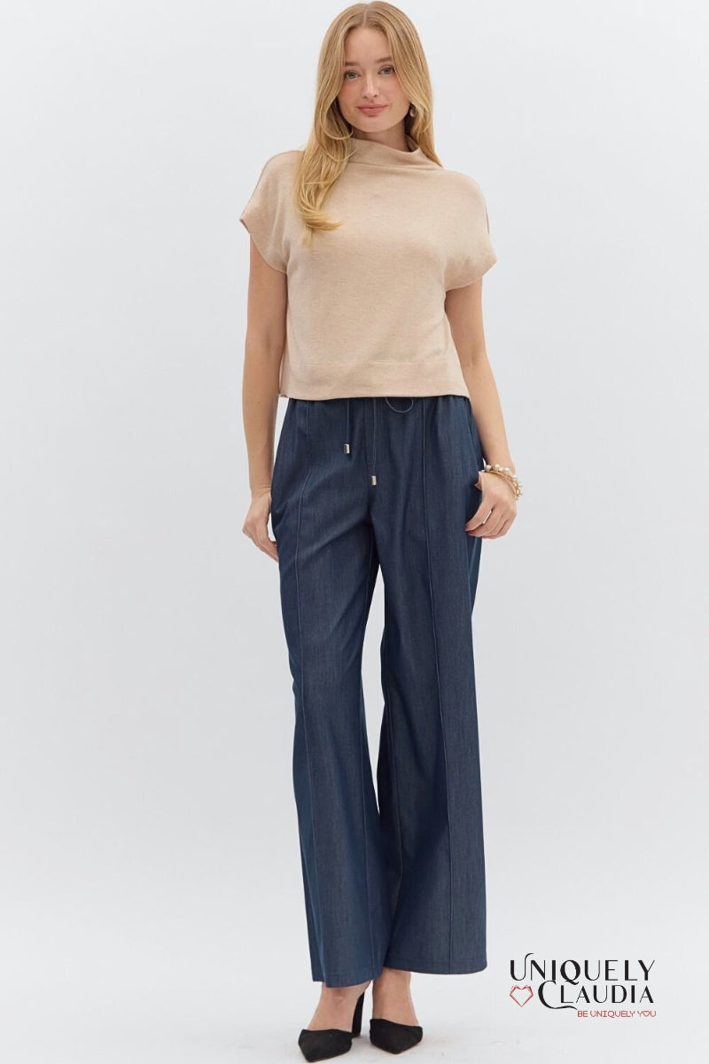 Woman wearing a beige top and navy pants on a white background with 'Uniquely Claudia' branding.