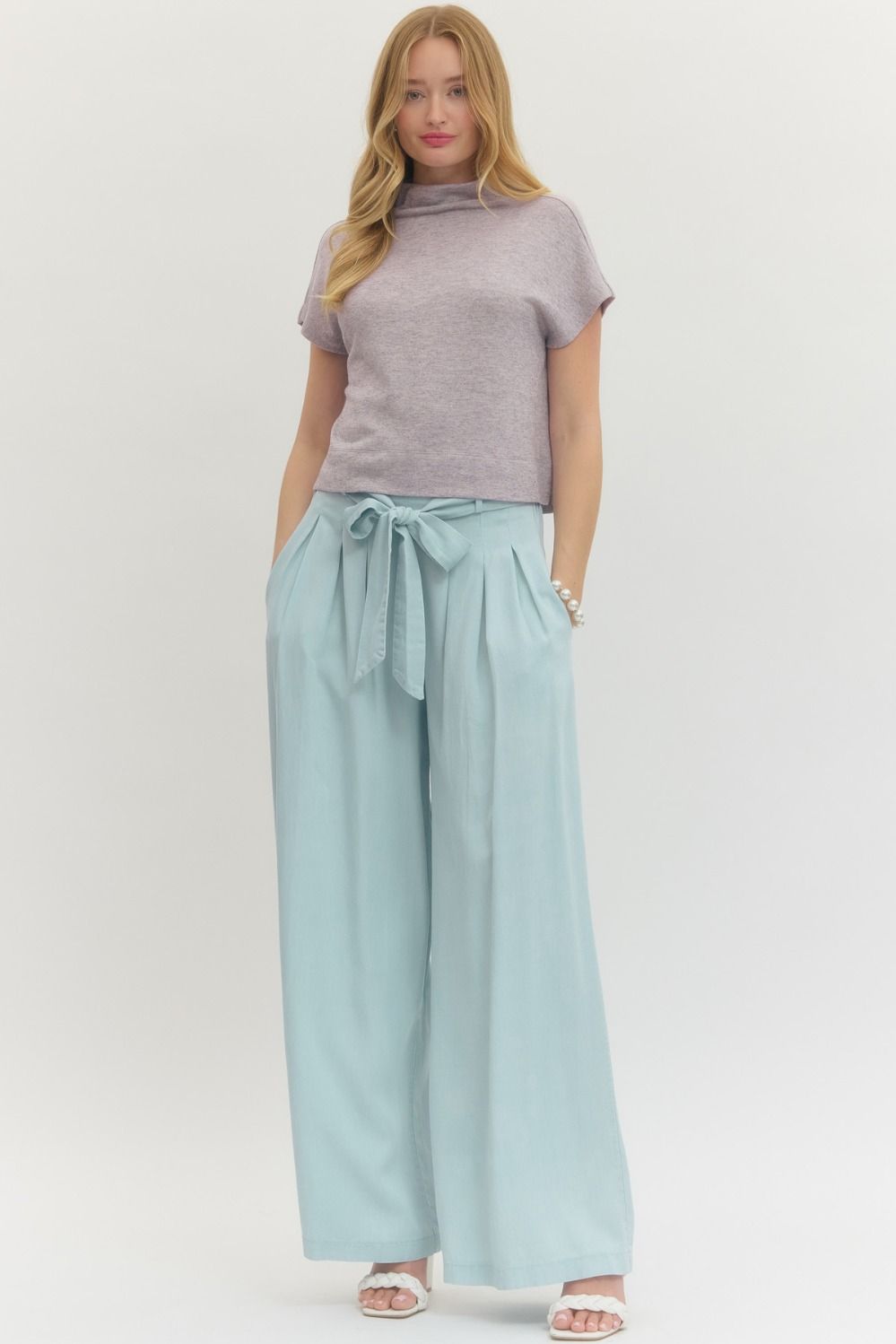 Woman wearing a gray top and light blue wide-leg pants on a white background