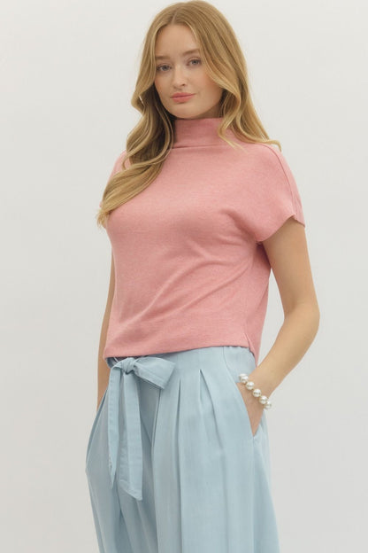 Woman wearing a pink top and light blue skirt against a plain background