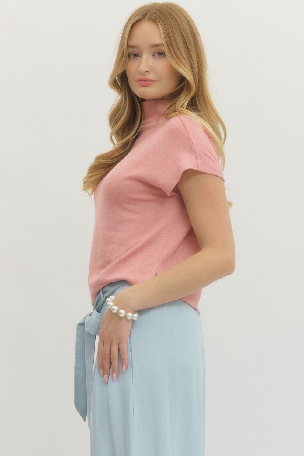 Woman wearing a pink top and light blue skirt on a plain background