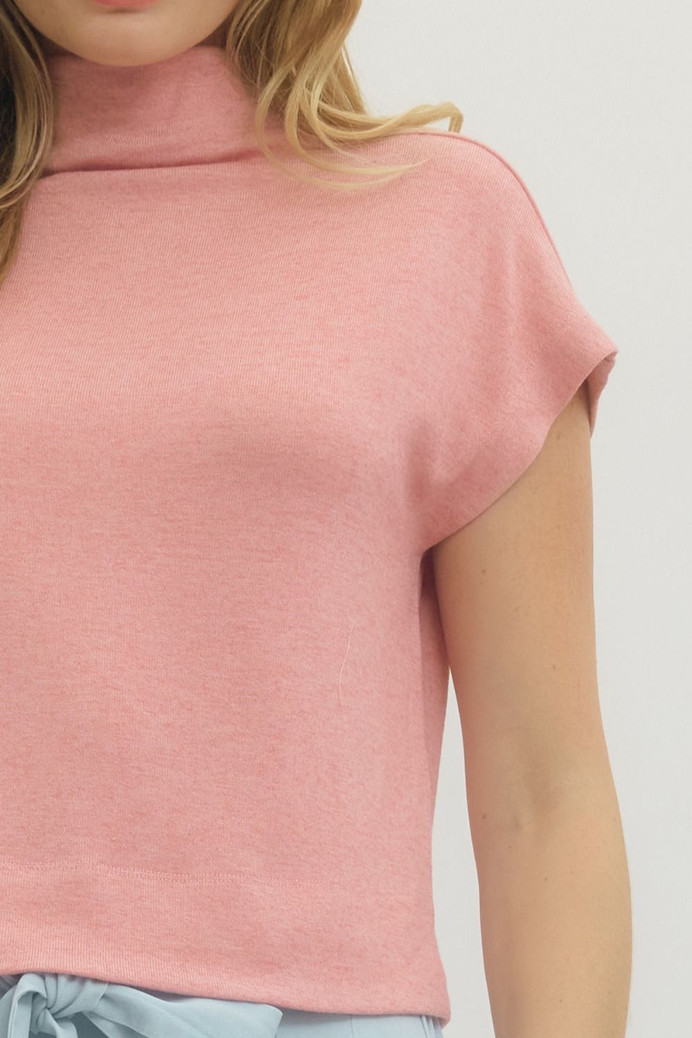 Close-up of a person wearing a pink sleeveless top on a light gray background