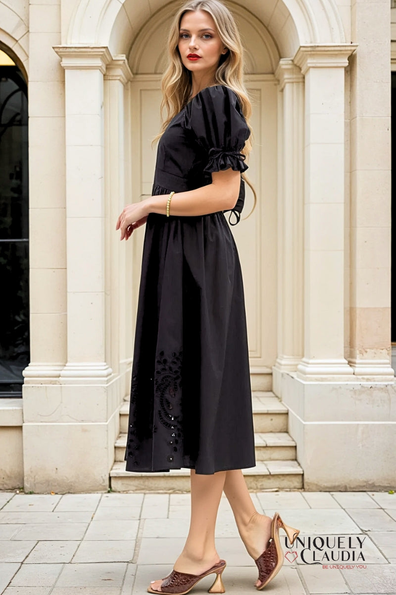 Woman in a black dress standing in front of a classical building entrance.