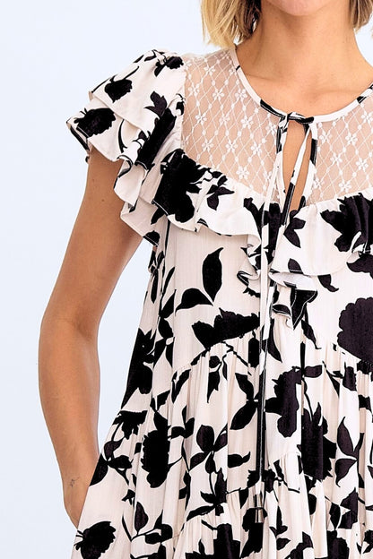 Woman wearing a black and white floral dress with sheer overlay on a light blue background
