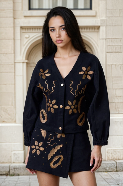 Woman wearing a black outfit with gold embroidery standing in front of a building.