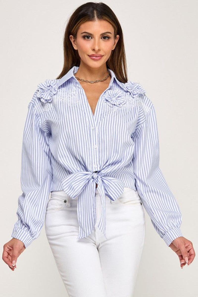 Woman wearing a blue and white striped shirt with ruffled shoulders on a plain background