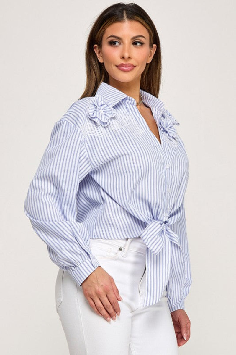 Woman wearing a blue and white striped shirt with a tie detail on a plain background