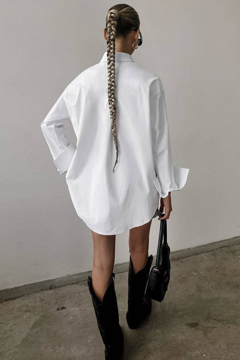 Person wearing a white oversized shirt and black boots against a plain wall.
