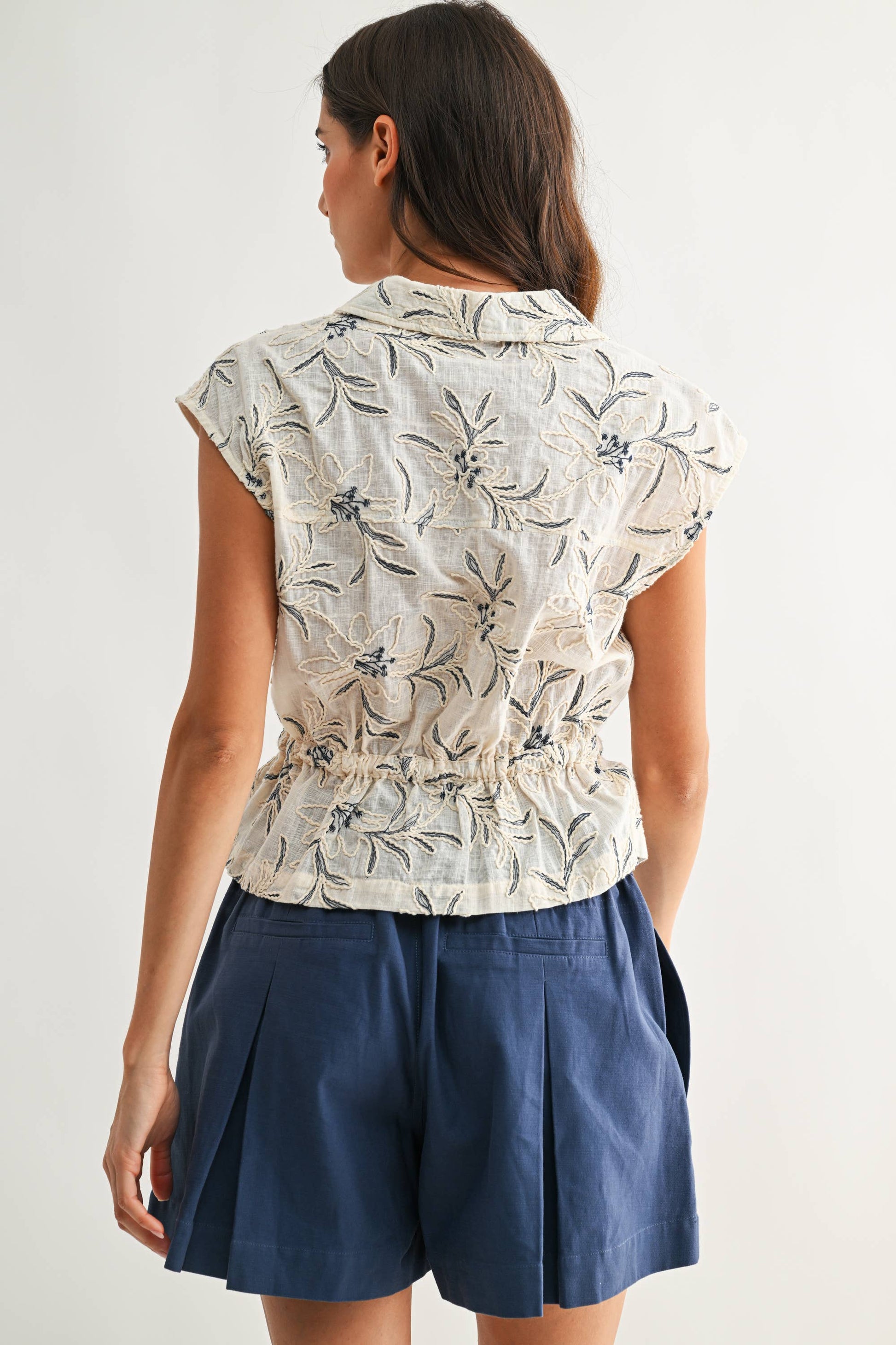 Woman wearing a floral blouse and navy shorts on a white background