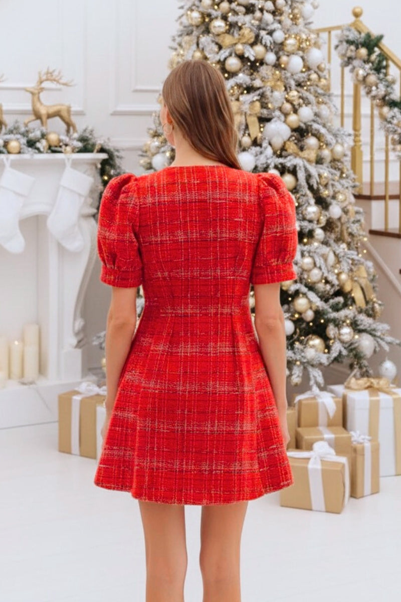 Woman in a red dress standing in front of a decorated Christmas tree and fireplace.