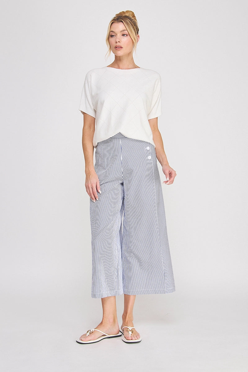 Woman wearing a white top and striped pants on a plain background