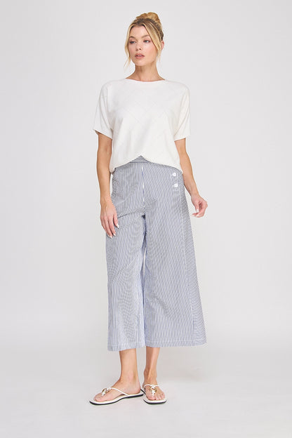Woman wearing a white top and striped pants on a plain background