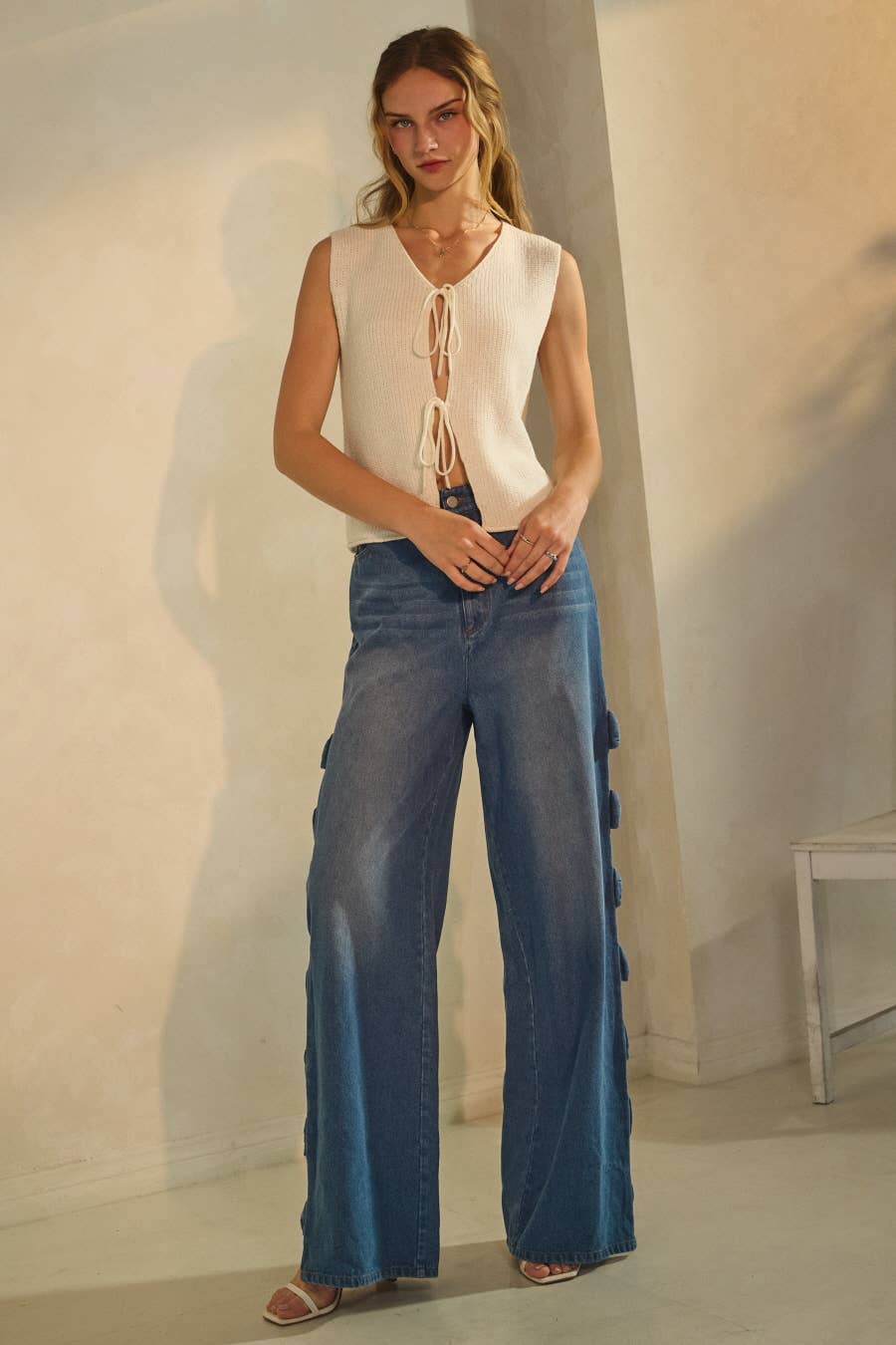 Woman wearing a sleeveless top and wide-leg jeans in a minimal setting
