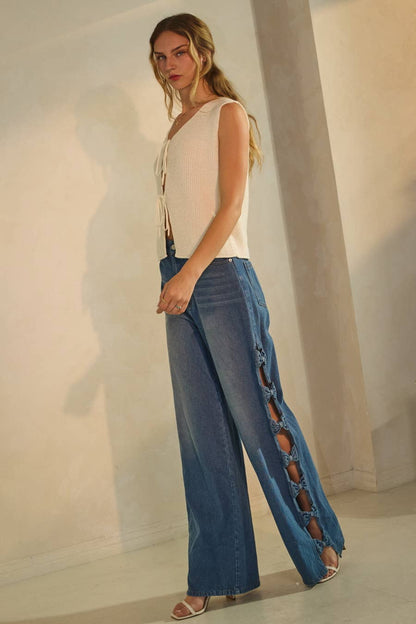 Woman wearing a white sleeveless top and blue jeans with cut-out sides against a plain background